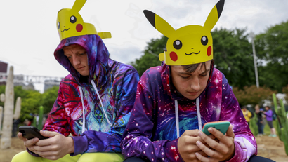 Two brothers in hoodies and Pikachu hats play Pokemon Go on their phones
