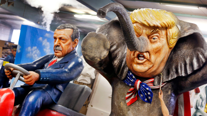 A worker poses with a brush in front of a figure depicting US President Donald Trump as an elephant and Turkish President Erdogan sitting on a bobby car during a press preview in a hall of the Main carnival club in Mainz, Germany, Tuesday, Feb. 21, 2017. The figure is part of various carnival floats of the Rose Monday procession in Mainz.