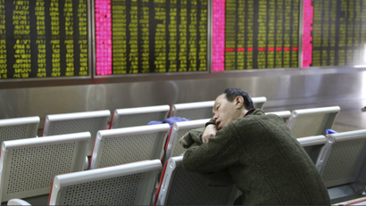 An man takes a nap in front of an electronic board showing stock information