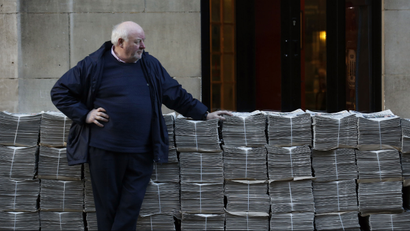 Man standing next to stacks of newspaper