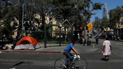 Pedestrians and cyclists pass by tents and tarps erected by homeless people in the skid row area of downtown Los Angeles, California