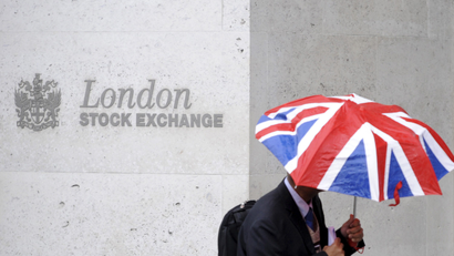 A worker shelters from the rain as he passes the London Stock Exchange in the City of London.
