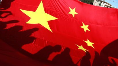 Participants cast shadows on a giant Chinese national flag before the start of the Beijing Marathon on Tiananmen Square in Beijing Sunday, Oct. 16, 2011. (AP Photo/Ng Han Guan