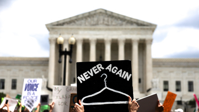 Abortion rights demonstrators protests outside the United States Supreme Court. One sign says "Never Again" over a drawing of a wire hanger.