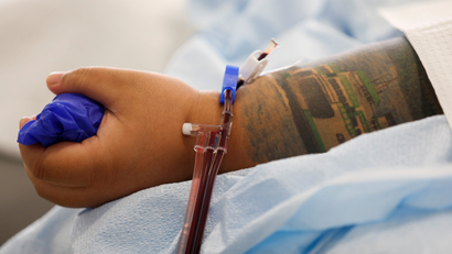 A person with a tattoo on their arm donates plasma while squeezing on a ball.