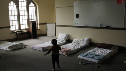 in a church, several bed mats are laid out for people to sleep on. The silhouette of a child stands in front of them.