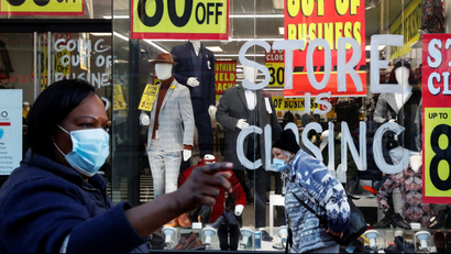 A Black woman walks by a clothing store window advertising a closing sale with several signs saying 80% off.