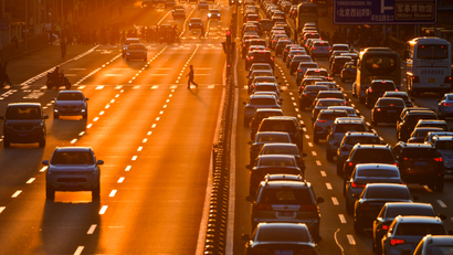 Pedestrian walks on a crossing next to cars in the traffic on a main road during sunset in Beijing