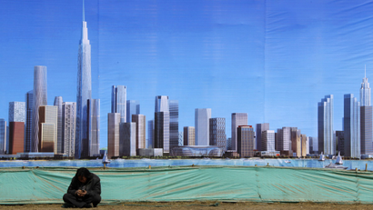 A worker rests in front of a billboard displaying an artist's impression of the new business district of Binhai, located in the Yujiapu financial zone on the outskirts of the city of Tianjin March 2, 2011. Round-the-clock construction is transforming muddy ground into what officials boast will be the world?s largest financial zone, a monument to the ambitions that have driven China to dizzyingly fast growth. When the country?s leaders gather for their annual parliament in Beijing on Saturday, they will endorse plans to tap the brakes on the speeding economy, a shift that is needed to keep inflation and debt, under control for now, from becoming far more troublesome. But they need only make the one-hour trip to the financial district sprouting up in Tianjin to see how hard-driving local officials, cash-rich state-owned banks and the soaring aspirations of people seeking a better life are imperiling their designs for slower, steadier growth. REUTERS/David Gray