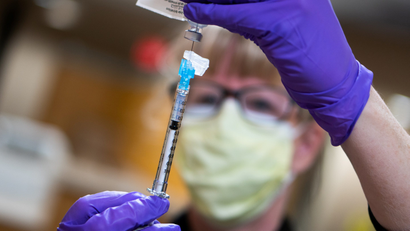 A person wearing purple gloves uses a syringe to remove a vaccine from its vial
