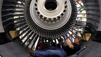 A GE Aviation employee lying on his back, building a massive engine.