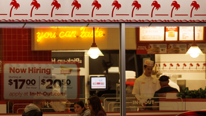 A "Now hiring" sign is displayed on the window of an IN-N-OUT fast food restaurant in Encinitas, California.