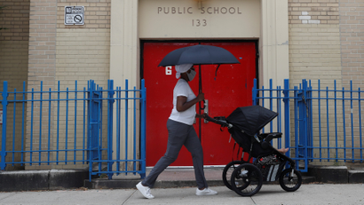 A woman pushes a baby in a cart past the entrance to Public School 133 in New York City