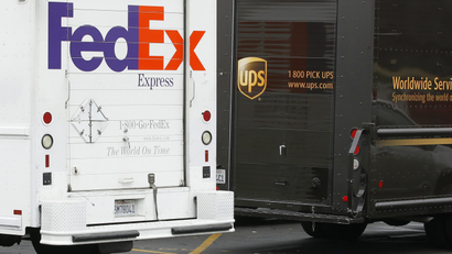 A FedEx truck is parked next to a UPS truck as both drivers make deliveries in downtown San Diego