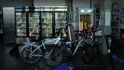 A delivery bike parked in front of fridges filled with grocery items in a warehouse.