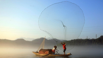 A fisherman casts his net to catch fish on Xin'an River in Jiande, Zhejiang province
