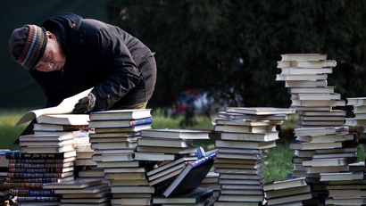 An elderly man browses one of books piled up on the grass for sale during the Winter Book Fair held at Ditan Park in Beijing, Sunday, Nov. 27, 2011.