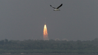 A Satellite Launch Vehicle carrying an orbiter, lifts off from a space center in India. In the foreground, a bird takes flight.