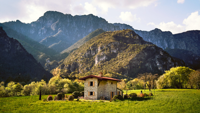 A small stone house set against the backdrop of mountains in the countryside