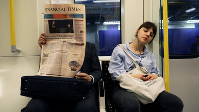 A woman sleeps on a train next to someone reading a newspaper