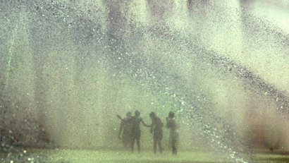 a fountain with eight shoots of water coming up and five blurry outlines of children playing in it.