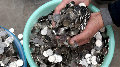 A person grabbing a handful coins from a bowl.