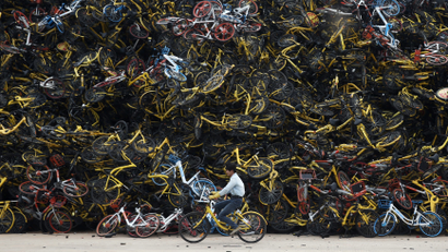 A worker rides a shared bicycle past piled-up shared bikes at a vacant lot in Xiamen, Fujian province, China December 13, 2017. Picture taken December 13, 2017. REUTERS/Stringer ATTENTION EDITORS - THIS IMAGE WAS PROVIDED BY A THIRD PARTY. CHINA OUT. - RC1C376F7180
