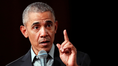 Image of Barack Obama in 2019 with his finger pointing up and microphone in one hand.