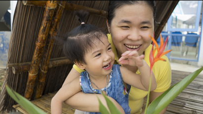 A OneSky caregiver shows a child a colorful flower and laughs with her