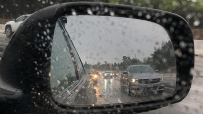 A view of rainy traffic through a car's right side mirror.