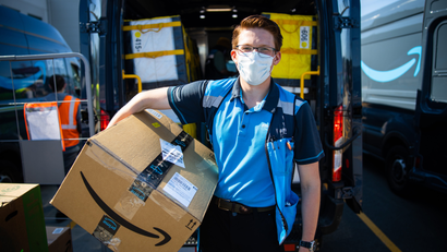 A delivery worker in a mask holds an Amazon Prime package