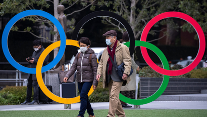 People wearing protective face masks are seen next to the Olympic rings
