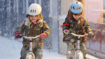 Two children ride their bicycles under heavy snow