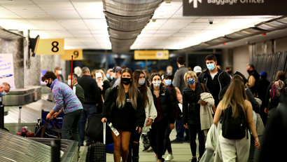 Travelers wearing face masks reclaim their luggage at the airport.