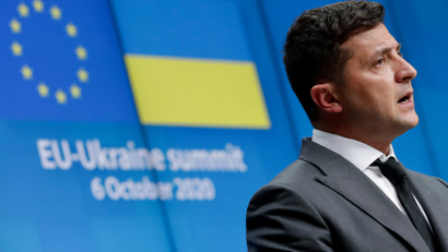 Ukrainian President Volodymyr Zelensky gives a press conference in front of a blue background with the EU and Ukrainian flags.