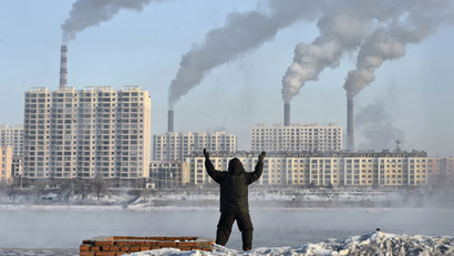 An elderly man exercises in the morning as he faces chimneys, China.