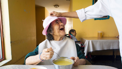 an older woman smiling as she eats her soup.