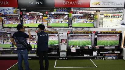People stand in front of a bank of television screens showing the World Cup.
