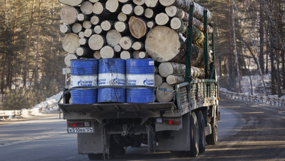 A truck carries wood and Gazprom Neft branded oil barrels.