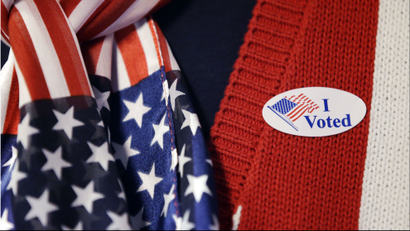 A close-up image of a person in a red vest and star-spangled scarf with an 'I Voted' sticker.