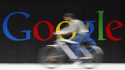 An image of an employee riding her bike past a logo next to the main entrance of the Google building in Zurich