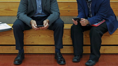 men in suits look at their phones while at a job fair