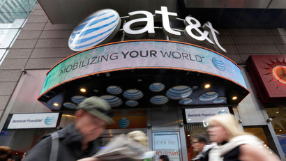 In this Oct. 21, 2014 photo, people pass an AT&T store in New York's Times Square. AT&T is being sued by the government over allegations it misled millions of smartphone customers who were promised unlimited data but had their Internet speeds cut by the company — slowing their ability to open web pages or watch streaming video. (AP Photo/Richard Drew)
