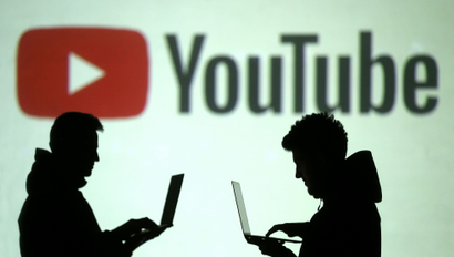 Silhouettes of mobile device users are seen next to a screen projection of Youtube logo in this picture illustration taken March 28, 2018.