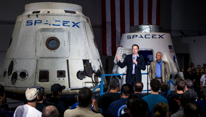 Elon Musk and a NASA exec talk about space exploration in front of a space capsule.