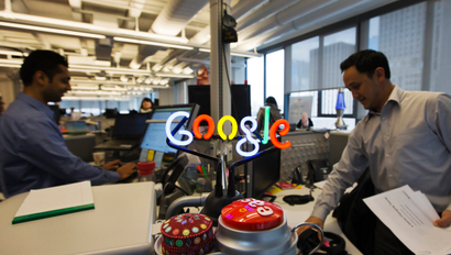 A neon Google logo is seen as employees work at the new Google office
