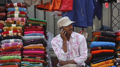A vendor speaks on his mobile phone as he waits for customers at his roadside shop selling clothes in Mumbai
