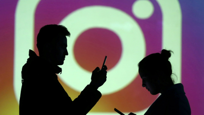 Silhouettes of mobile users are seen next to a screen projection of Instagram logo