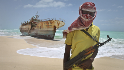 In this photo taken Sunday, Sept. 23, 2012, masked Somali pirate Hassan stands near a Taiwanese fishing vessel that washed up on shore after the pirates were paid a ransom and released the crew, in the once-bustling pirate den of Hobyo, Somalia. The empty whisky bottles and overturned, sand-filled skiffs that litter this shoreline are signs that the heyday of Somali piracy may be over - most of the prostitutes are gone, the luxury cars repossessed, and pirates talk more about catching lobsters than seizing cargo ships.