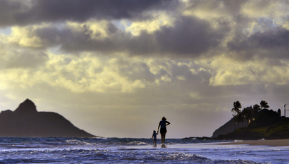 Anne Kllingshirn, of Kailua, Hawaii walks with her daughter Emma, 1, as storm clouds float overhead during the sunrise hours on Kailua Beach, in Kailua, Hawaii, Thursday morning Aug. 7, 2014. The National Weather Service downgraded Hurricane Iselle to a tropical storm about 50 miles before it was expected to make landfall early Friday in the southern part of Hawaii's Big Island. By 2 a.m. Hawaii Standard Time on Friday, the storm was swirling about 10 miles from the Kau coastline. (AP Photo/Luci Pemoni